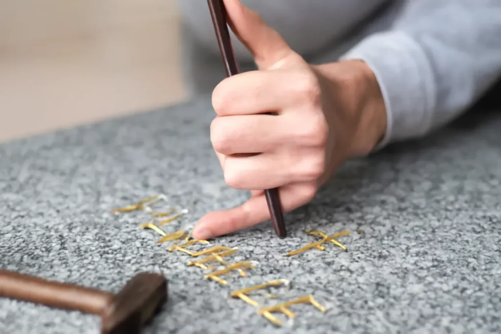 Dorure à la feuille d'or réalisée à la main sur une plaque funéraire en granit.