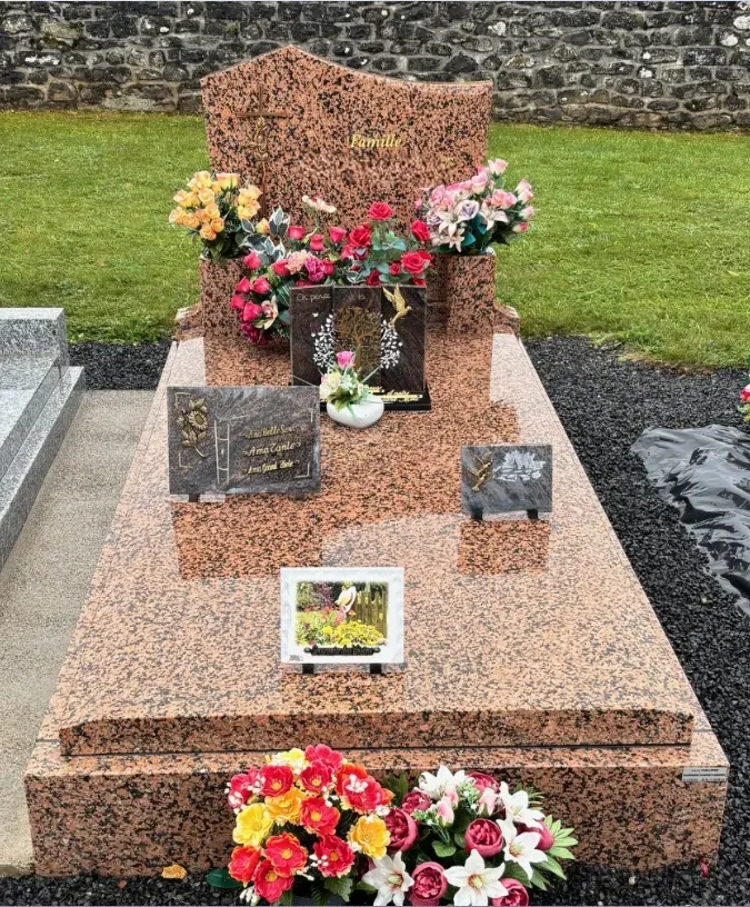 Monument funéraire en granit rose poli orné de plaques et de compositions florales.